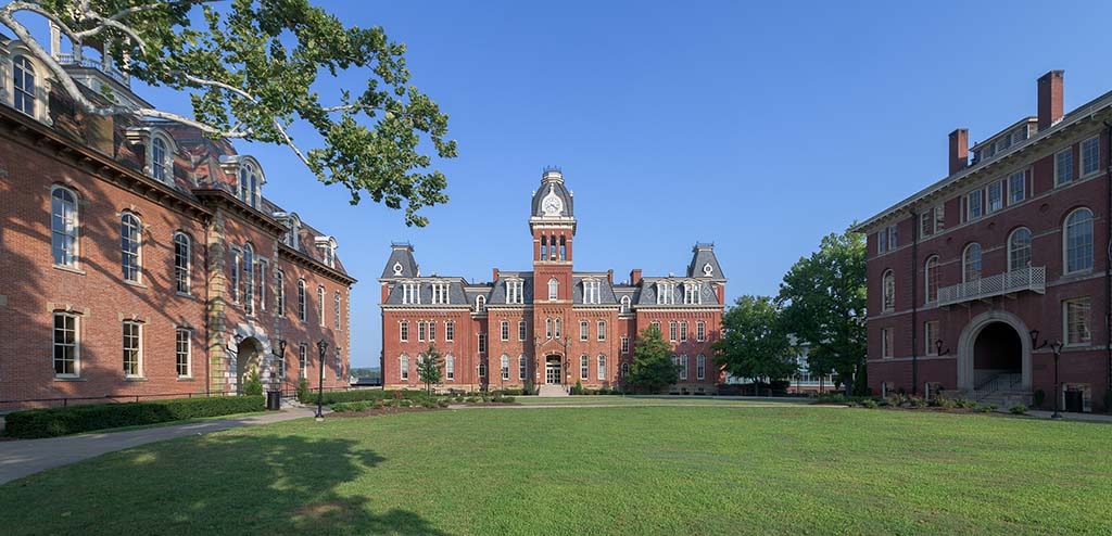 Exterior of a brick college building with a clock tower and a green grassy courtyard.